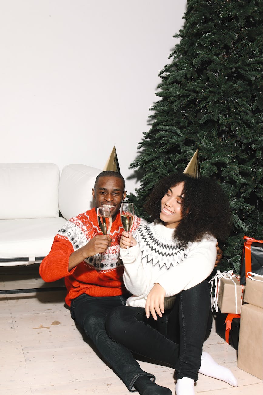 couple sitting beside a christmas tree drinking wine